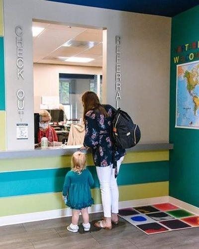 Woman and child at library check-out counter; colorful accents, world map on wall, child behind counter.