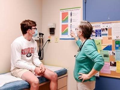 A healthcare provider points at a chart while speaking to a patient sitting on an exam table in a clinic.