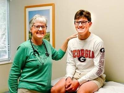 Doctor in green scrubs with stethoscope, touches smiling patient's shoulder. Office visit.