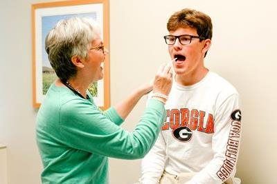 Medical professional examining a patient's throat. The patient opens mouth. The office has a framed picture on the wall.