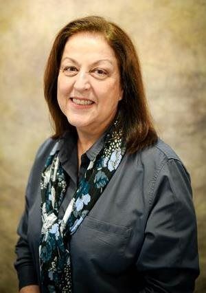 Woman in blue shirt and floral scarf smiling, looking at the camera.
