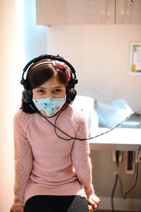 Girl wearing headphones and mask in an exam room, likely for a hearing test.