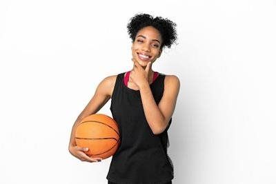 Woman in athletic wear holding a basketball, smiling, and touching her chin.