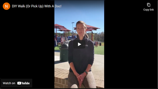 Woman outside in black shirt and brown leggings, sitting with a park in the background.
