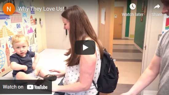 A woman and child in a brightly decorated room. The woman reaches down to the child, who sits on the floor.