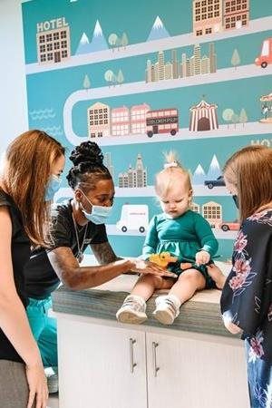 Medical staff examining a child in a doctor's office with travel-themed wall decor.