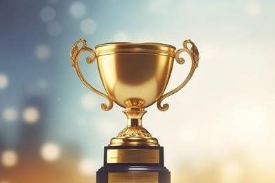 Gold trophy on a dark base, with handles, against a blurred background.