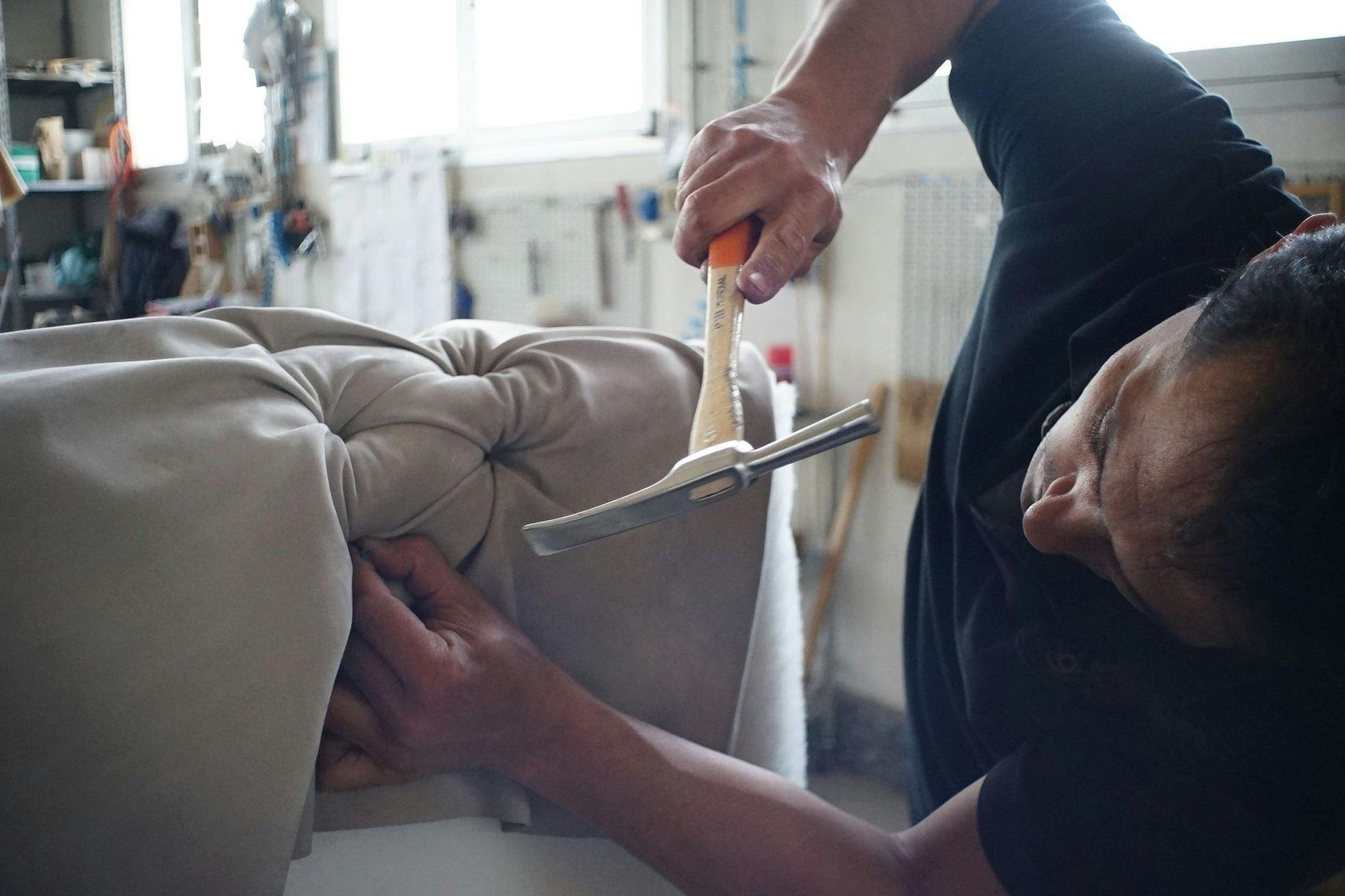 Person using a hammer and upholstery tool to work on a button-tufted furniture piece.