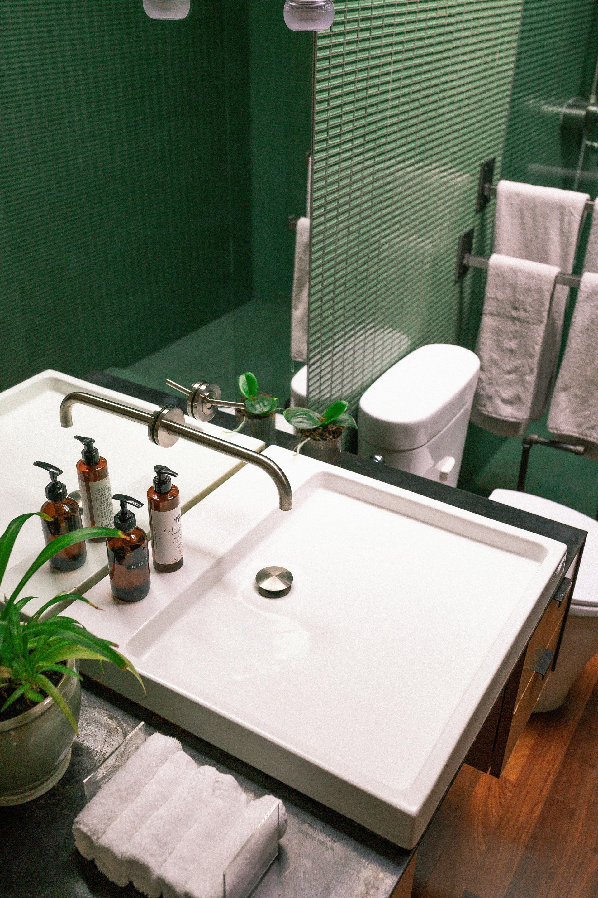 Modern bathroom with white rectangular sink, green mosaic tile wall, and white towels.