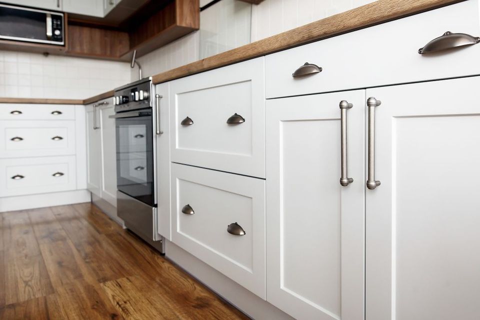 White kitchen cabinets with brushed nickel hardware and a wooden countertop.  A built-in oven is visible, and the floor is wood.