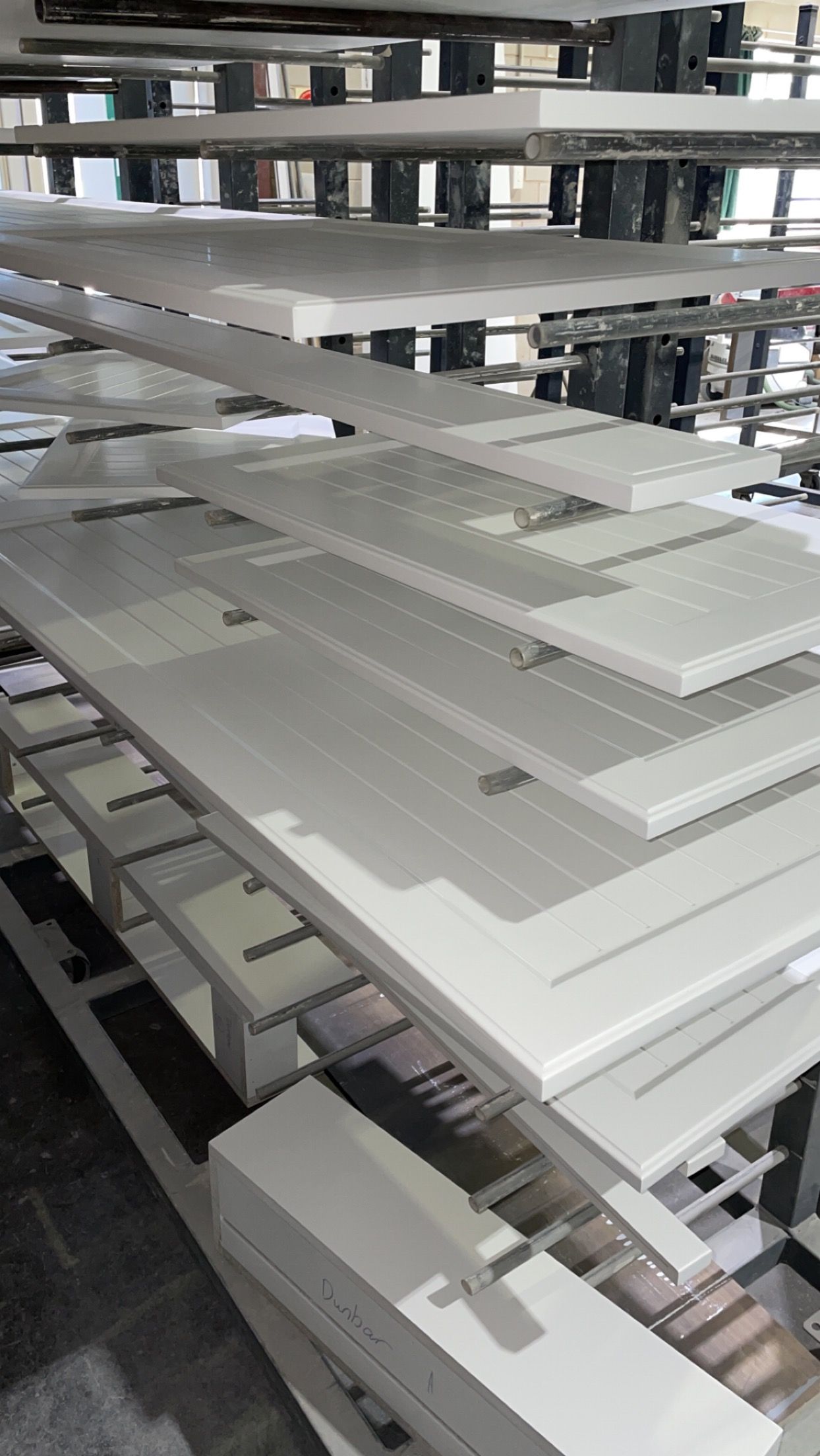 White doors stacked on shelves in a factory or warehouse. The doors have paneling and are awaiting assembly.