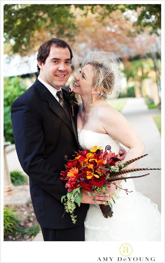 The bride and groom are posing for a picture and the bride is holding a bouquet of flowers.