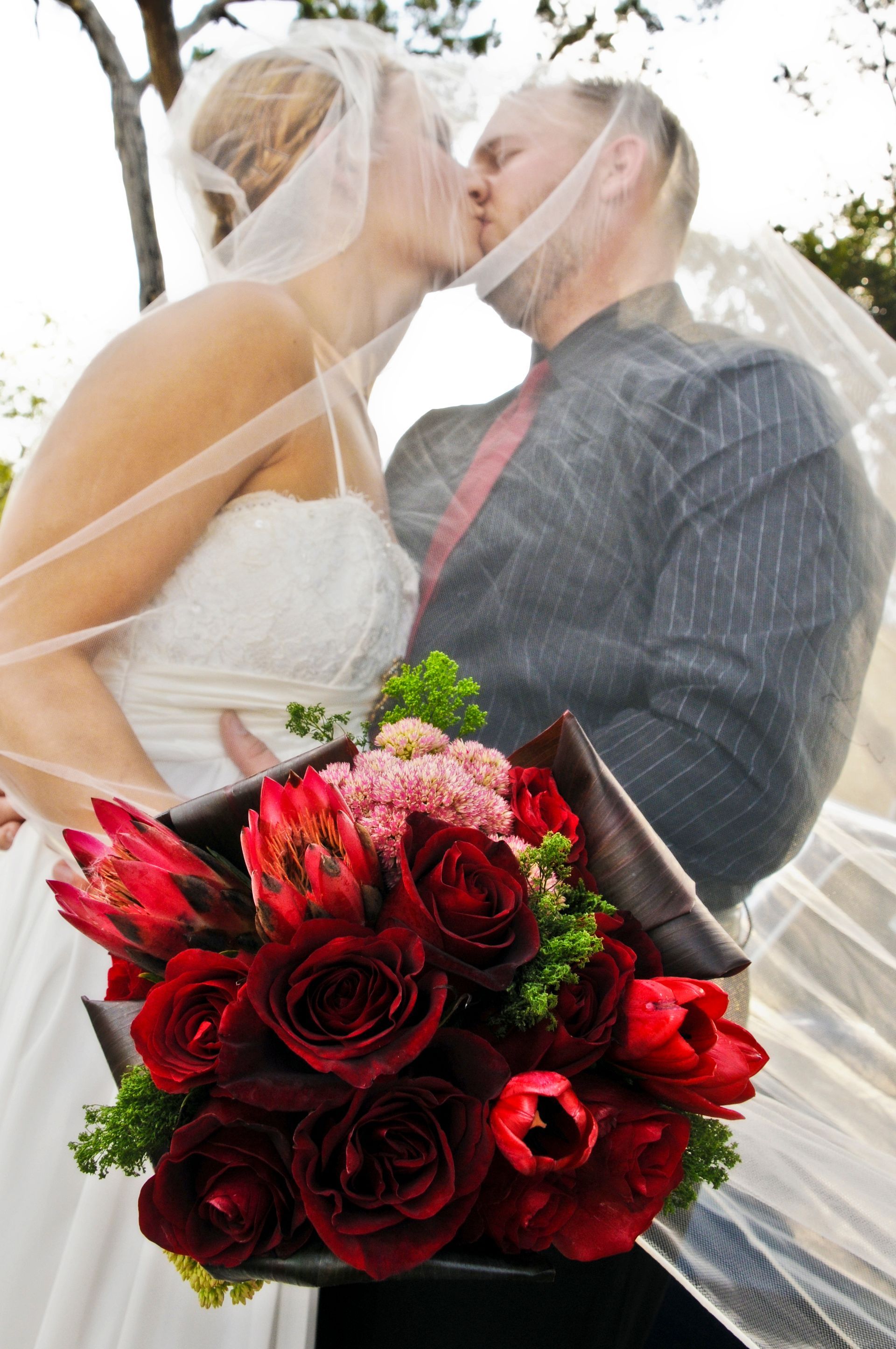 A bride and groom kissing while holding a bouquet of red roses