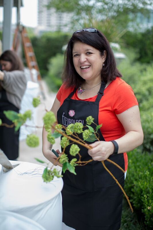 A woman in an apron is holding a branch of green flowers.