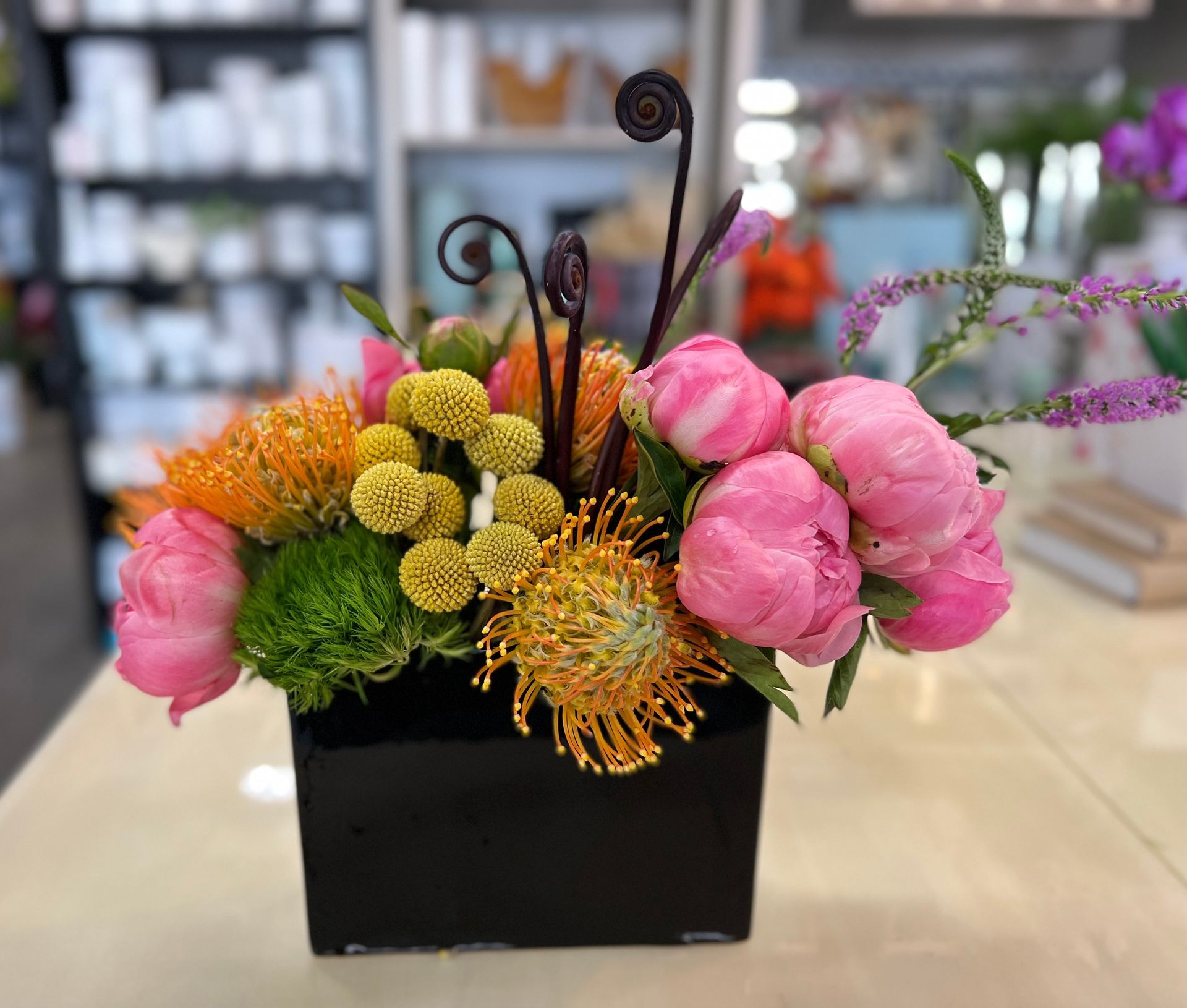 A black vase filled with pink and yellow flowers is sitting on a table.