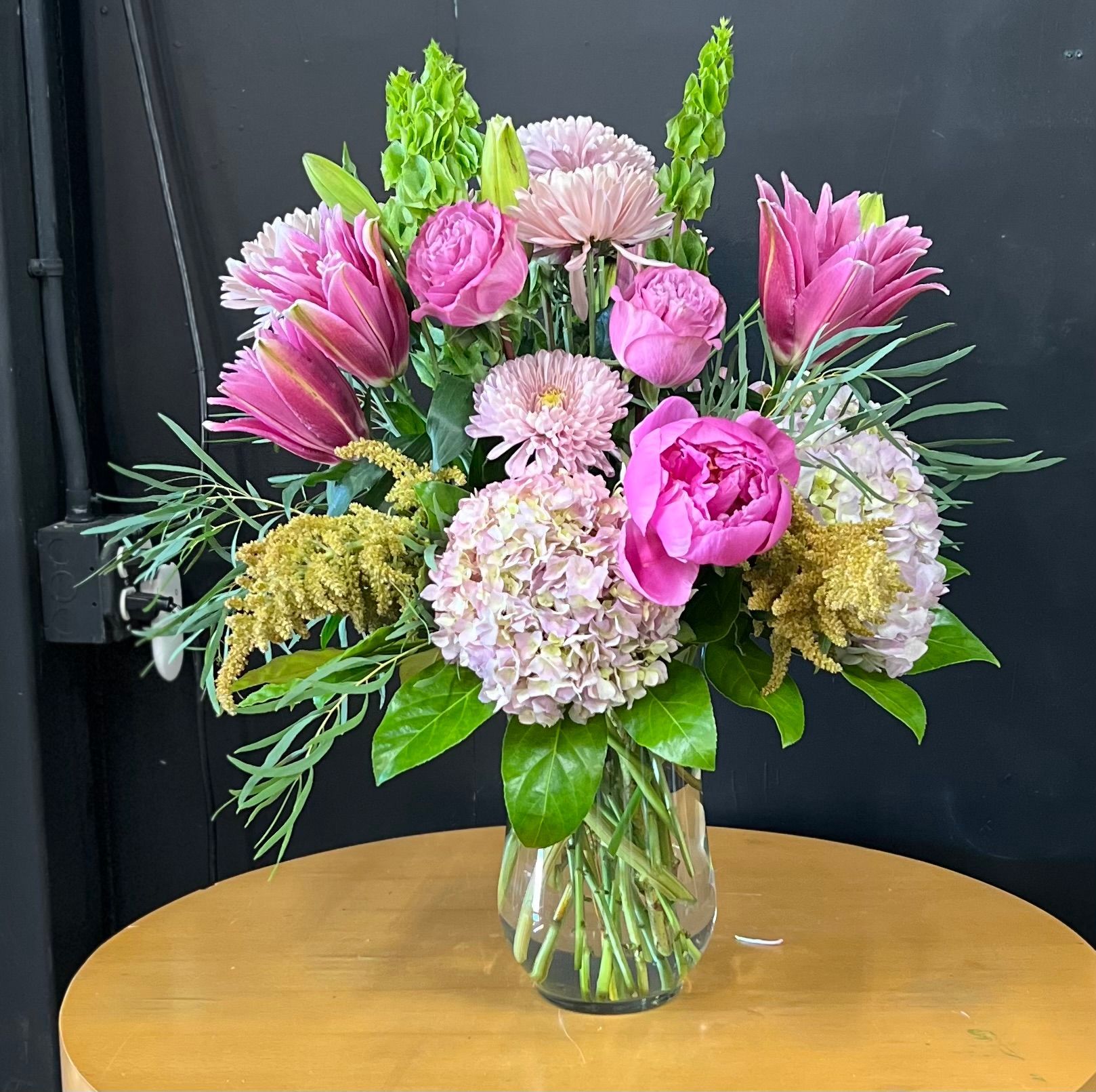A vase filled with pink flowers is sitting on a wooden table.