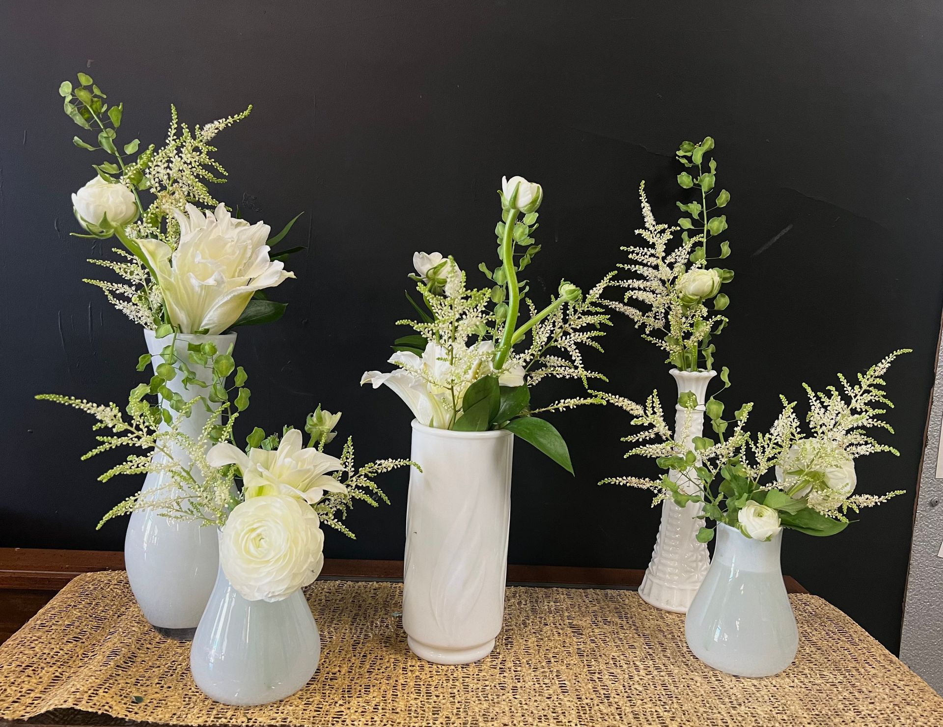 A group of white vases filled with white flowers on a table.