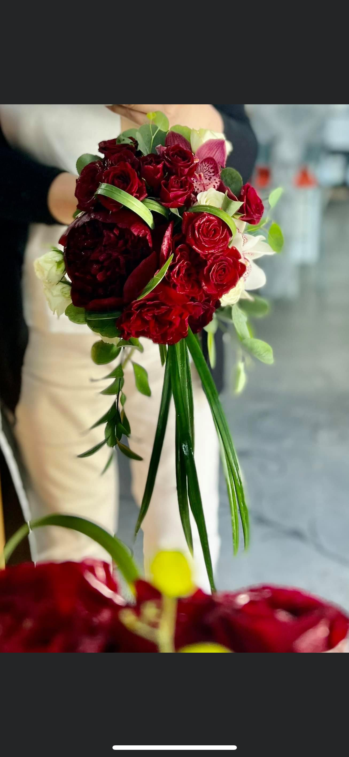 A person is holding a bouquet of red roses and greenery.