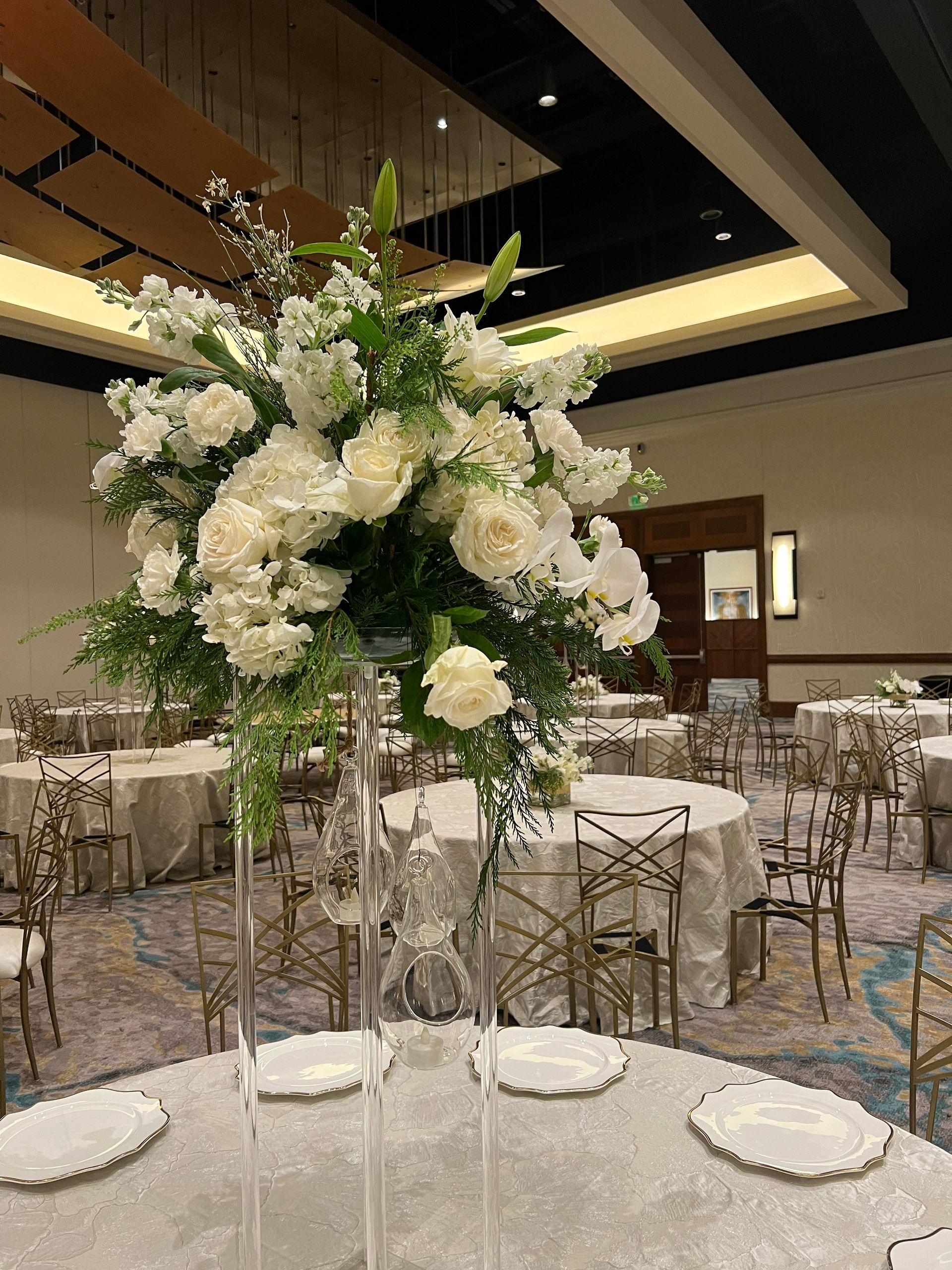 A tall vase filled with white flowers is on a table in a large room.