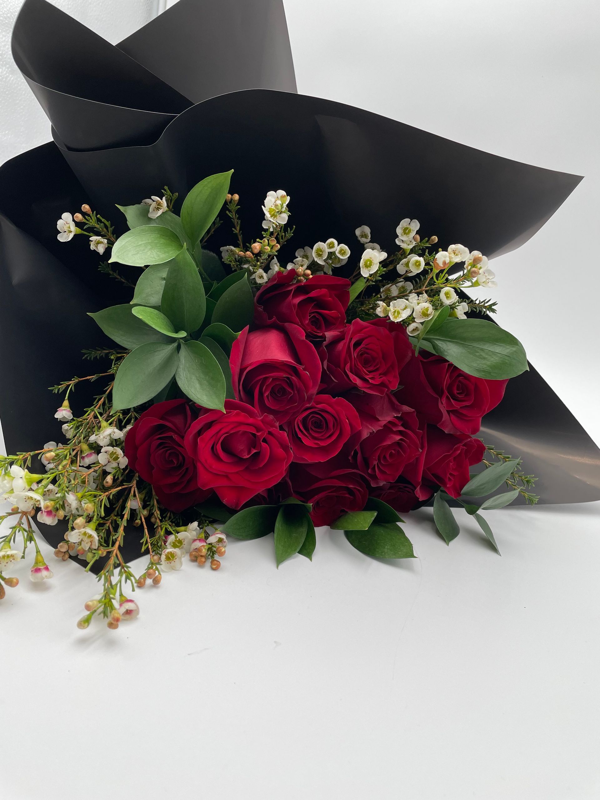 A bouquet of red roses wrapped in black paper on a white surface.
