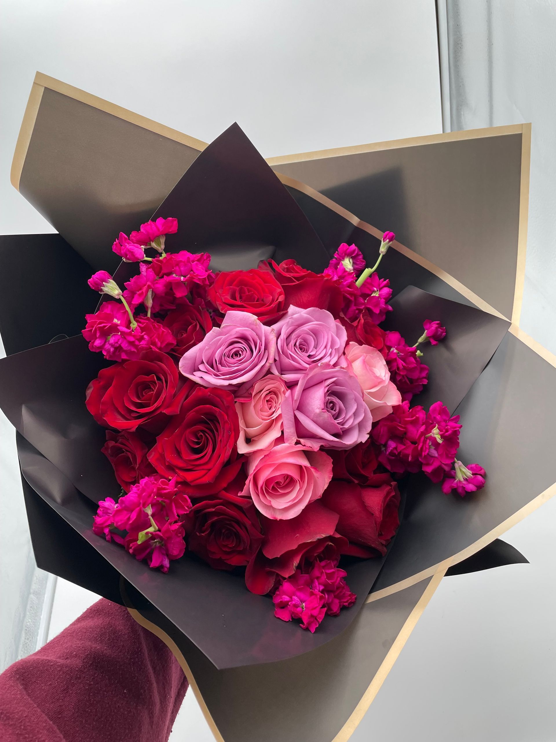 A person is holding a bouquet of red and pink roses