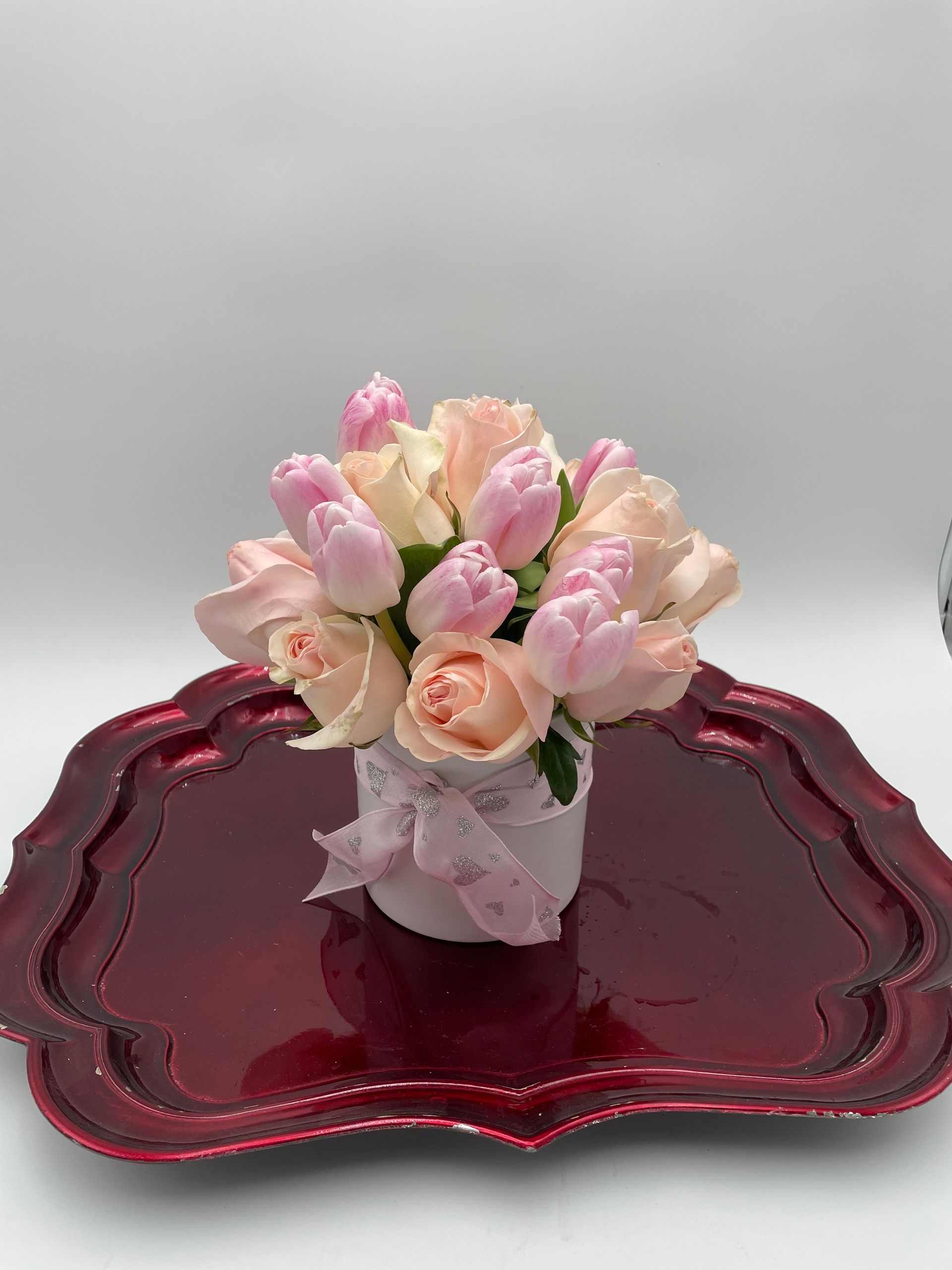 A vase filled with pink roses and tulips is sitting on a red tray.