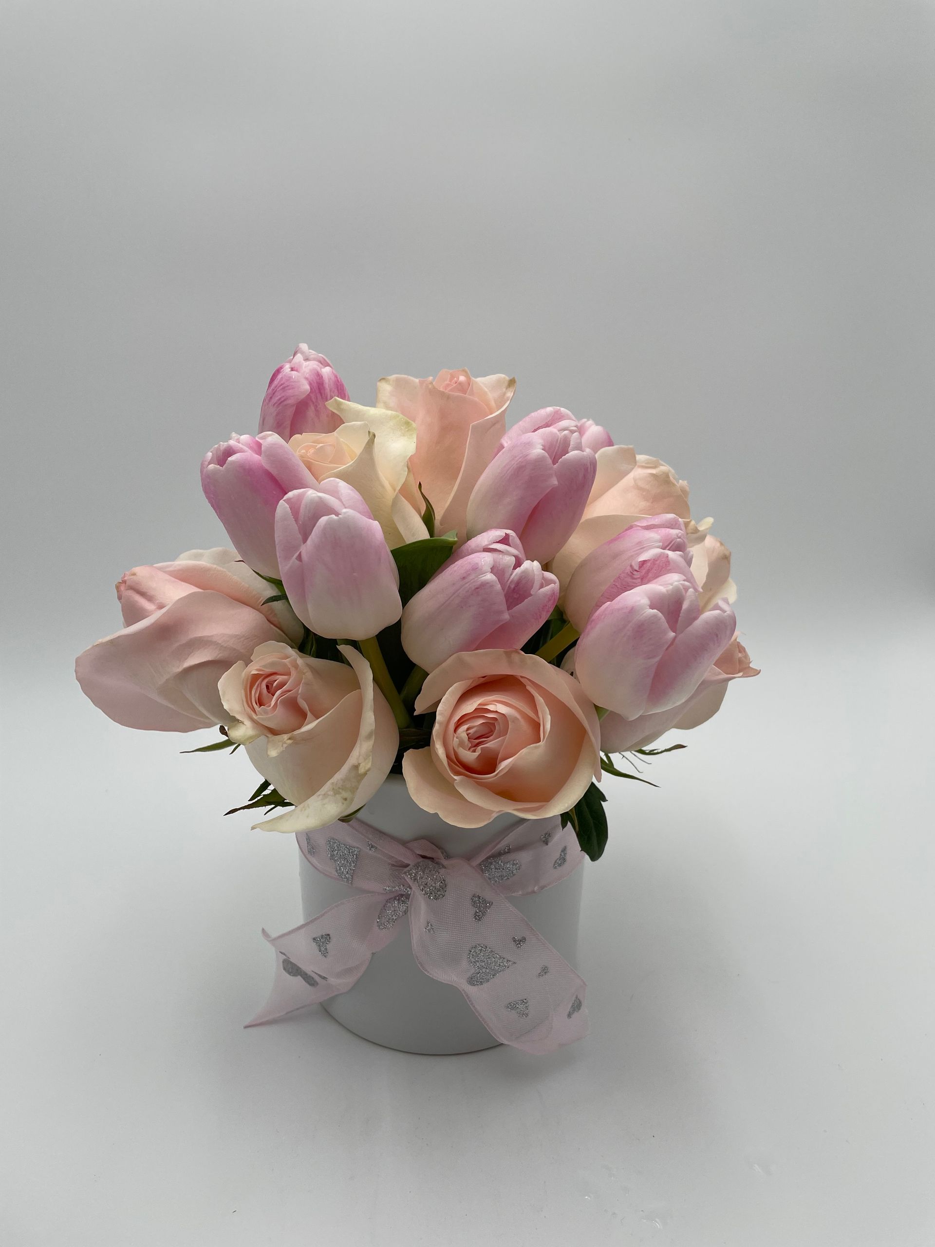 A vase filled with pink roses and tulips on a white surface.