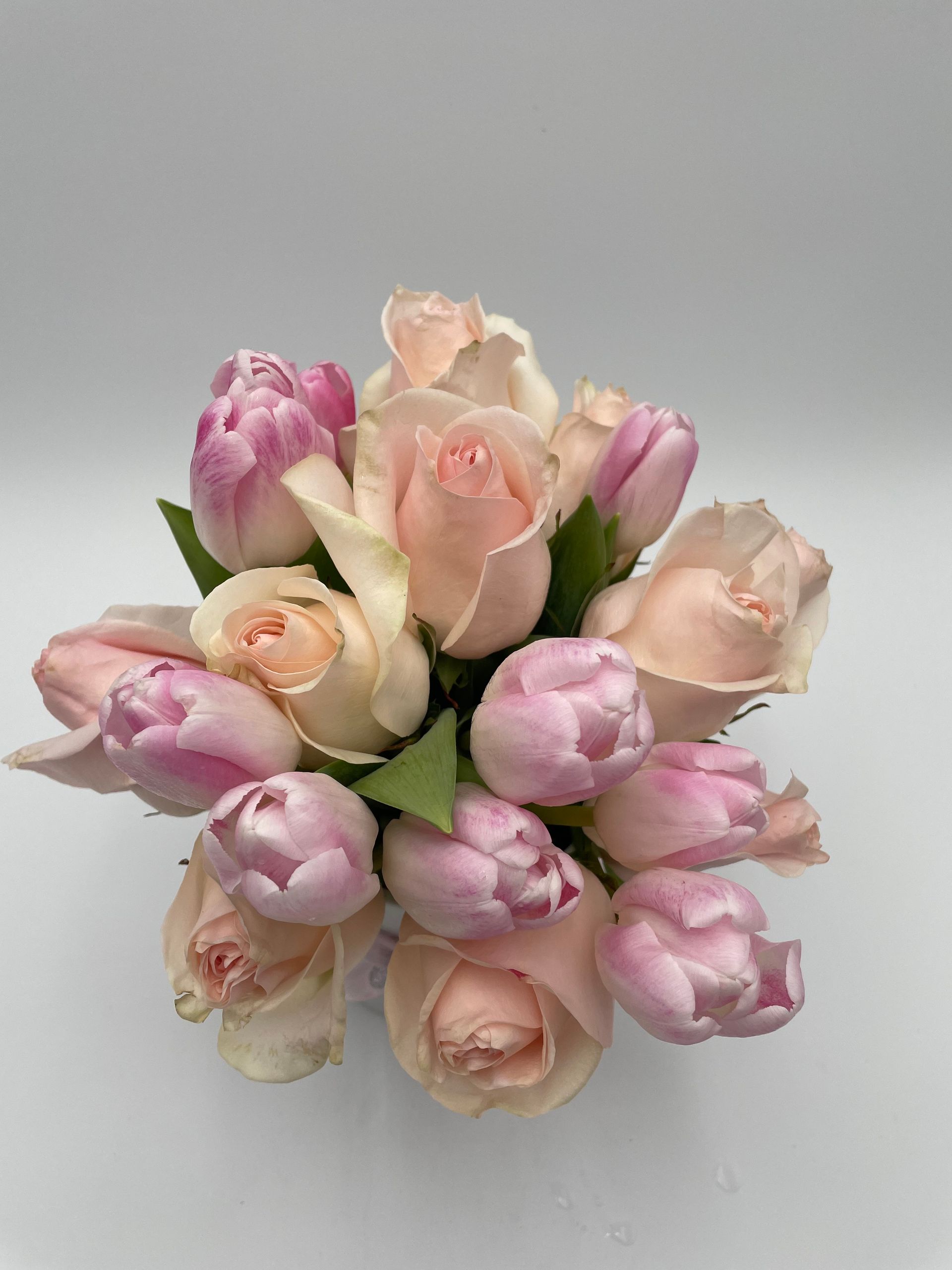 A bouquet of pink roses and tulips on a white surface