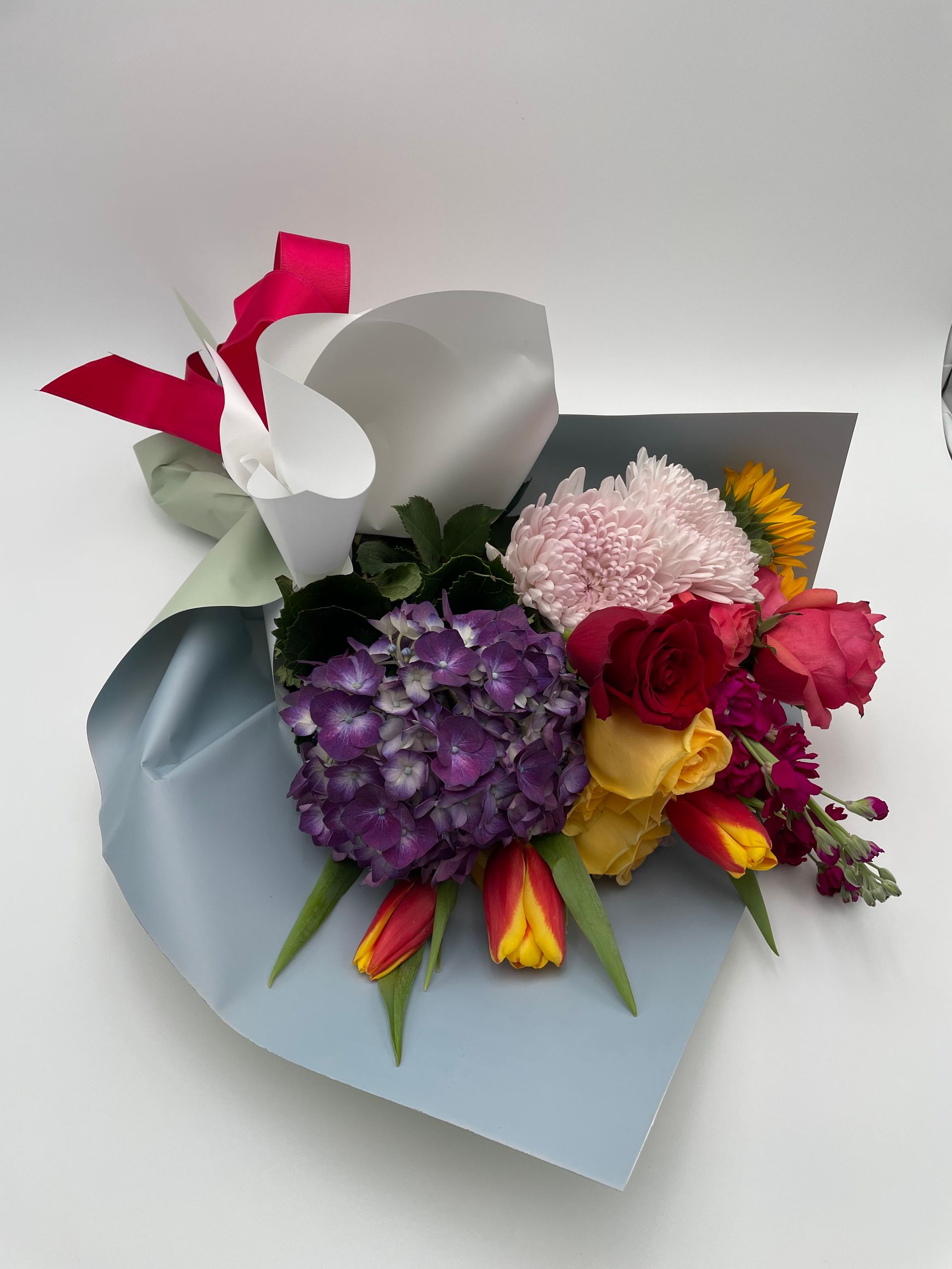 A bouquet of flowers wrapped in blue paper on a white surface.