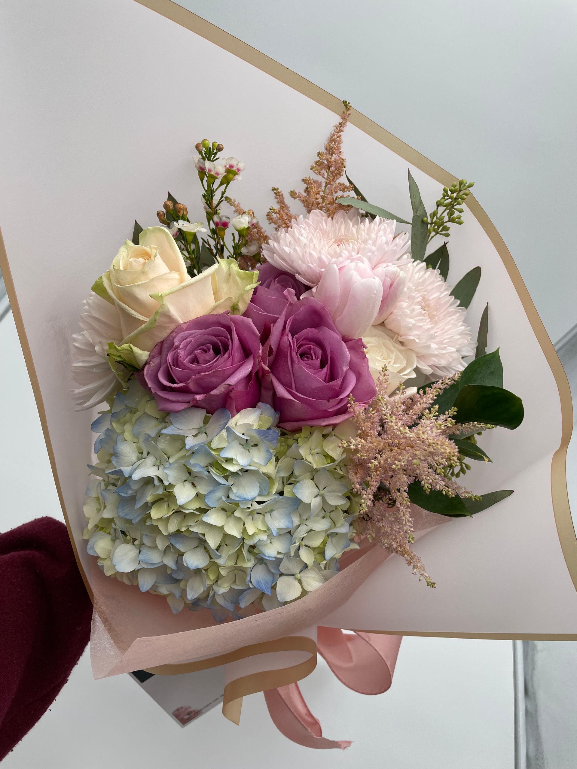 A person is holding a bouquet of flowers wrapped in pink paper.