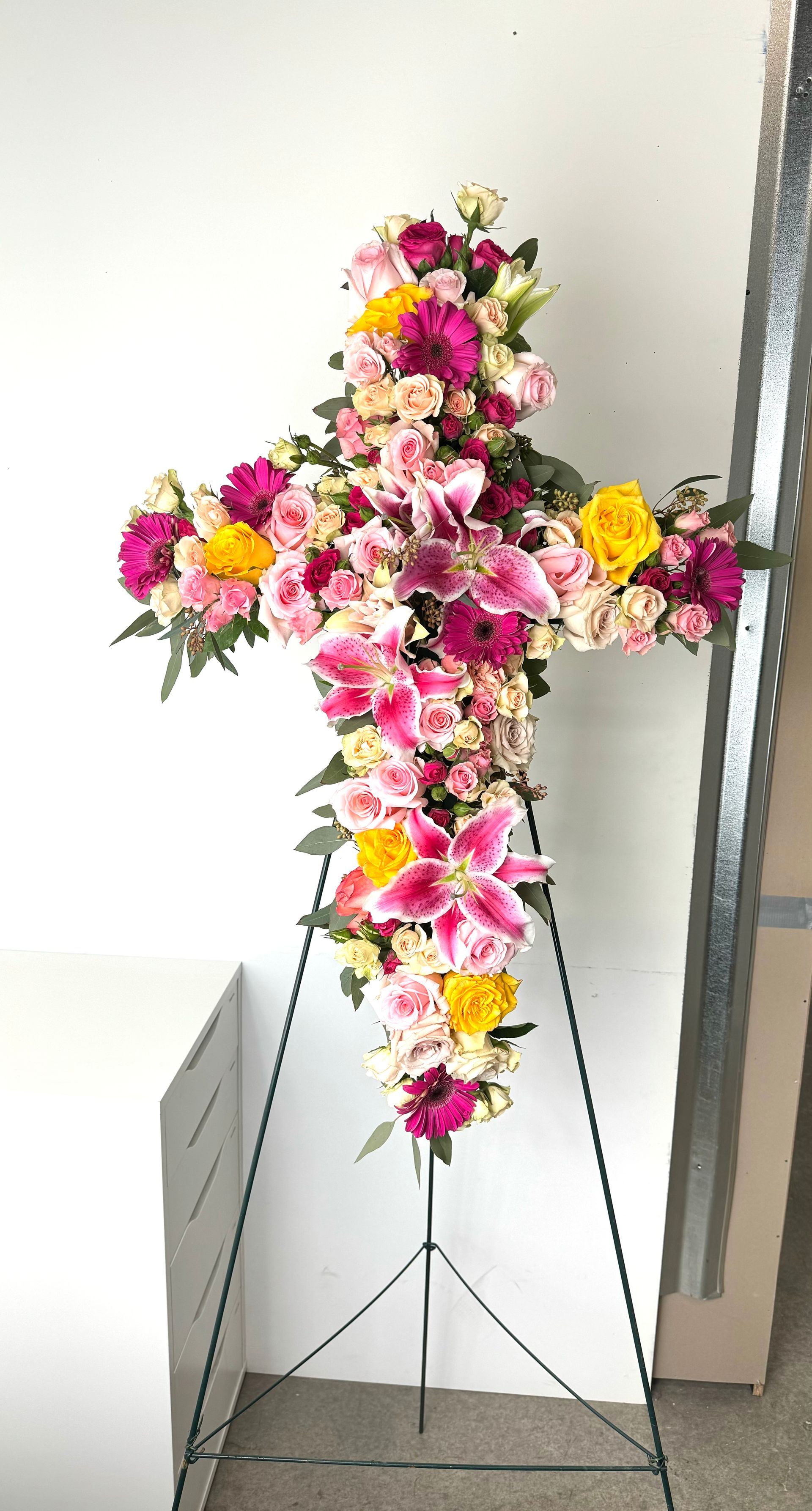 A cross made of pink and yellow flowers on a stand.