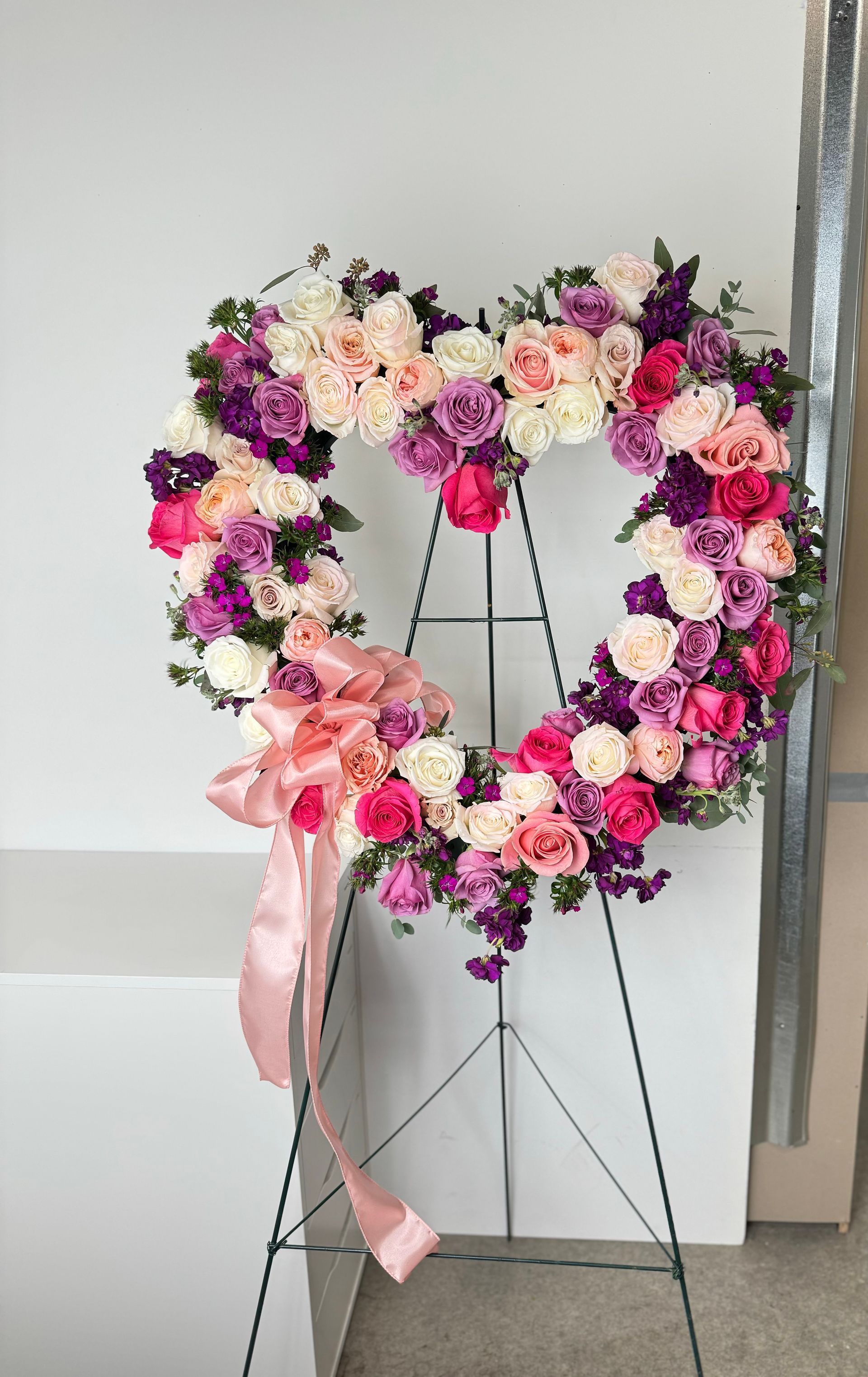 A heart shaped wreath of pink and purple flowers on a stand.
