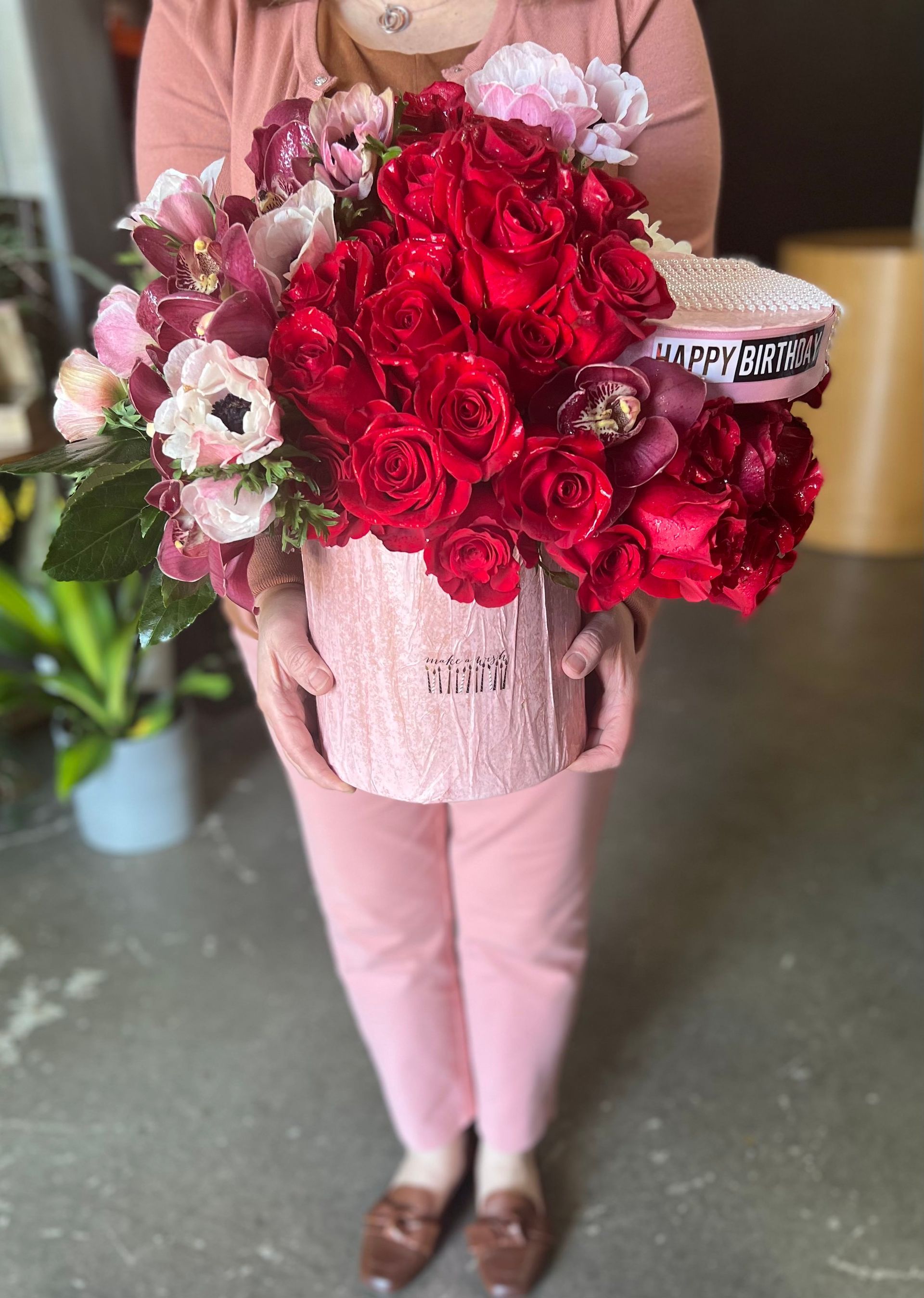 A woman is holding a pink box filled with red roses.