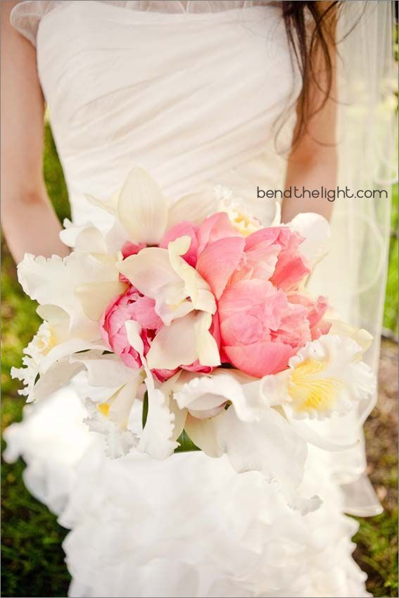A bride in a white dress is holding a bouquet of pink and white flowers.