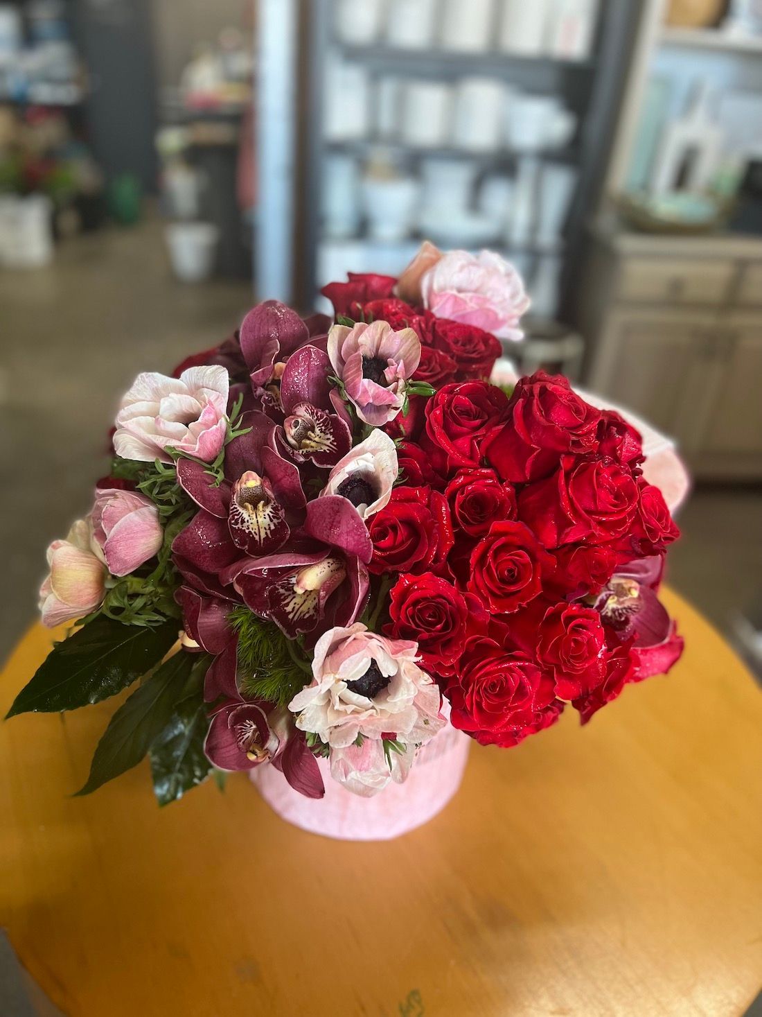 A pink vase filled with red roses and pink flowers is sitting on a wooden table.