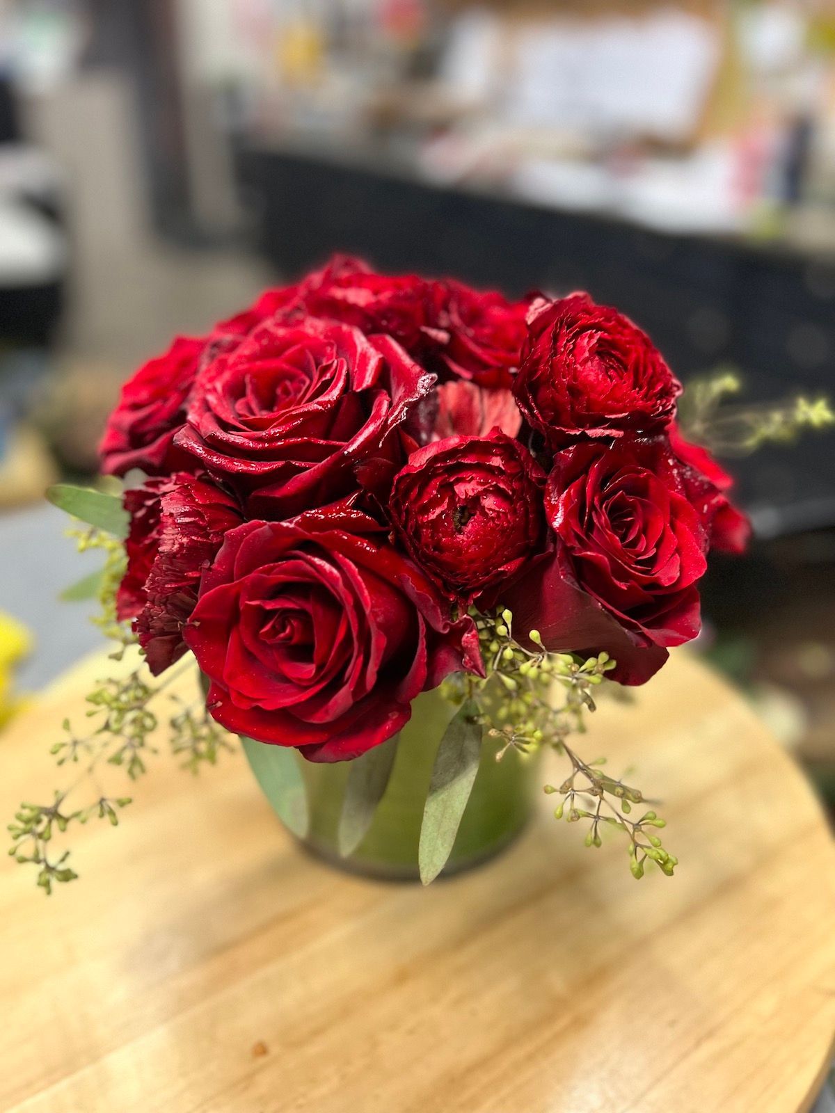 A vase filled with red roses is sitting on a wooden table.