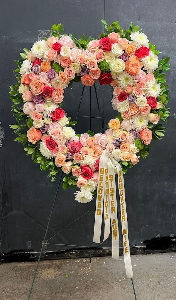 A heart shaped wreath of flowers is sitting on a stand.