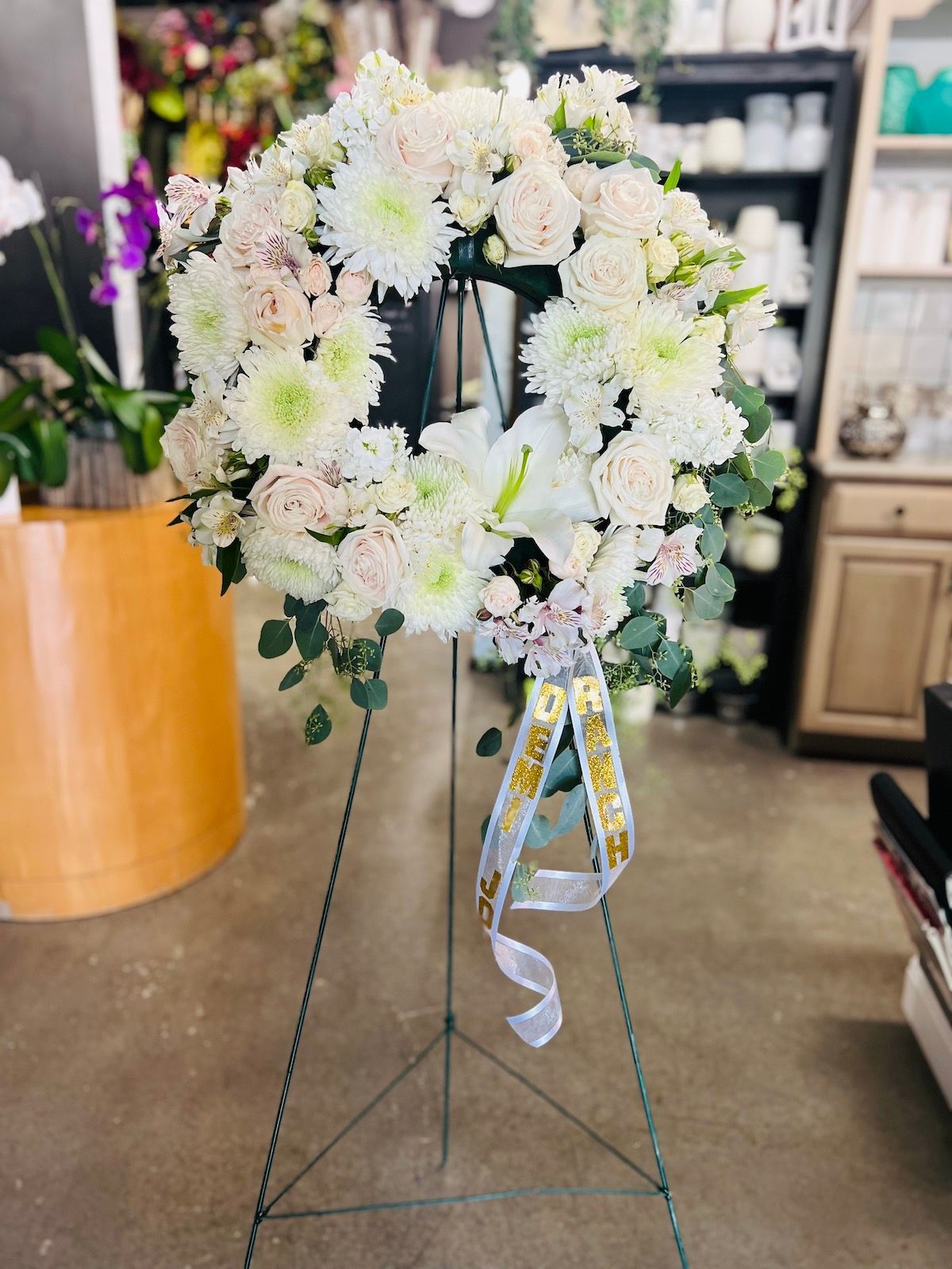 A wreath of white flowers is sitting on a metal stand in a room.