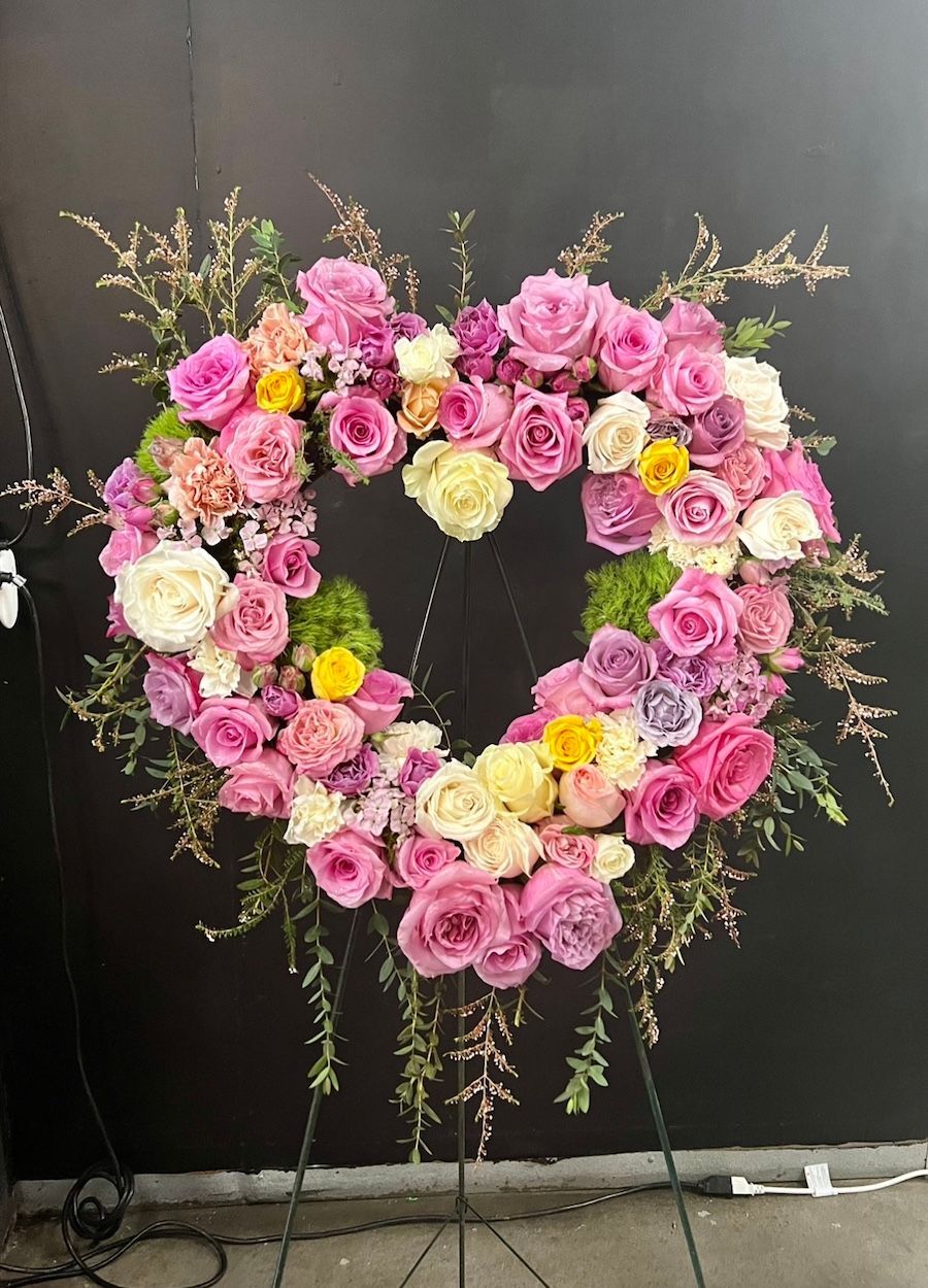 A heart shaped wreath made of pink and yellow roses on a stand.