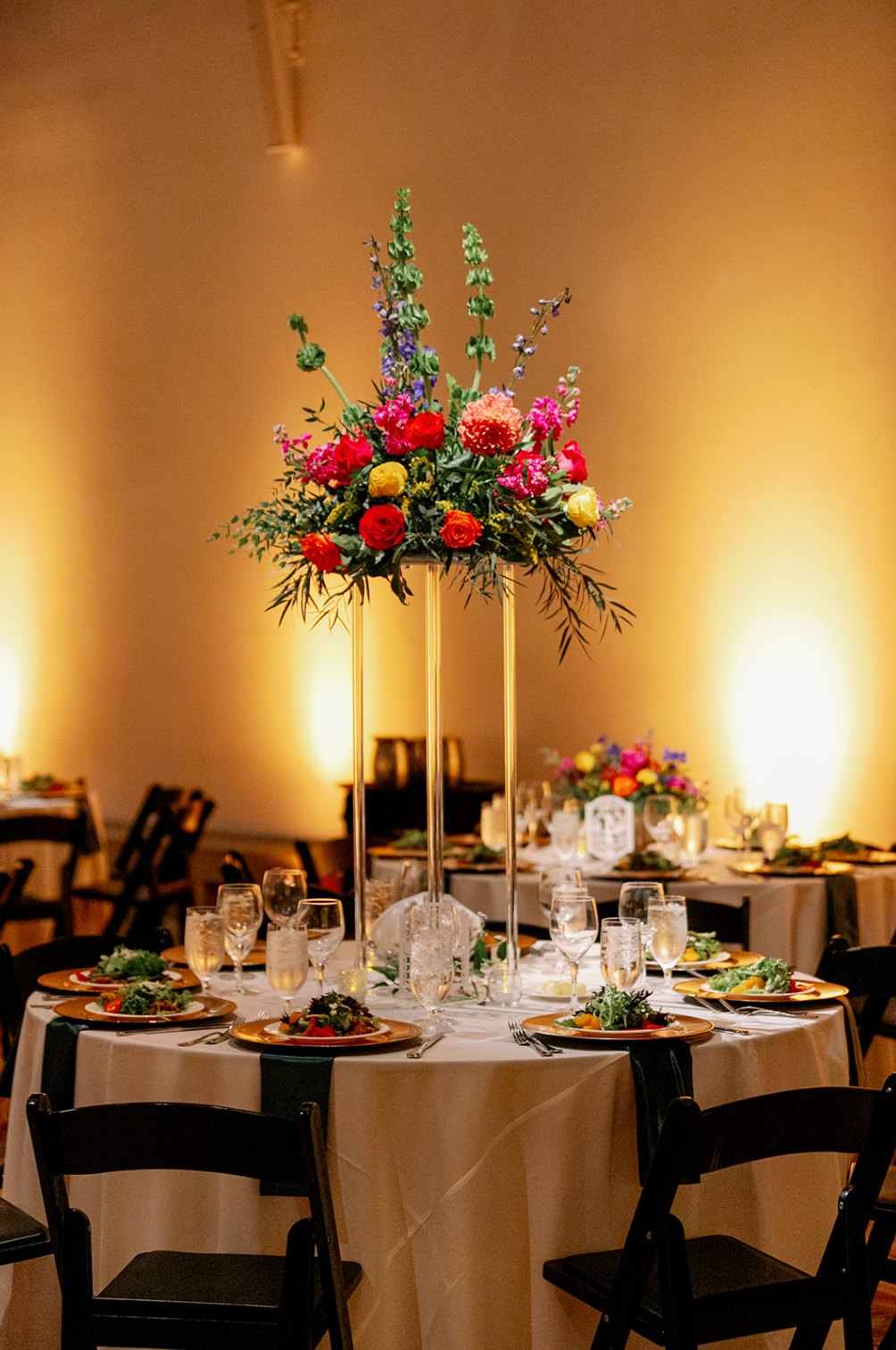 A table set for a wedding reception with a tall vase filled with flowers.