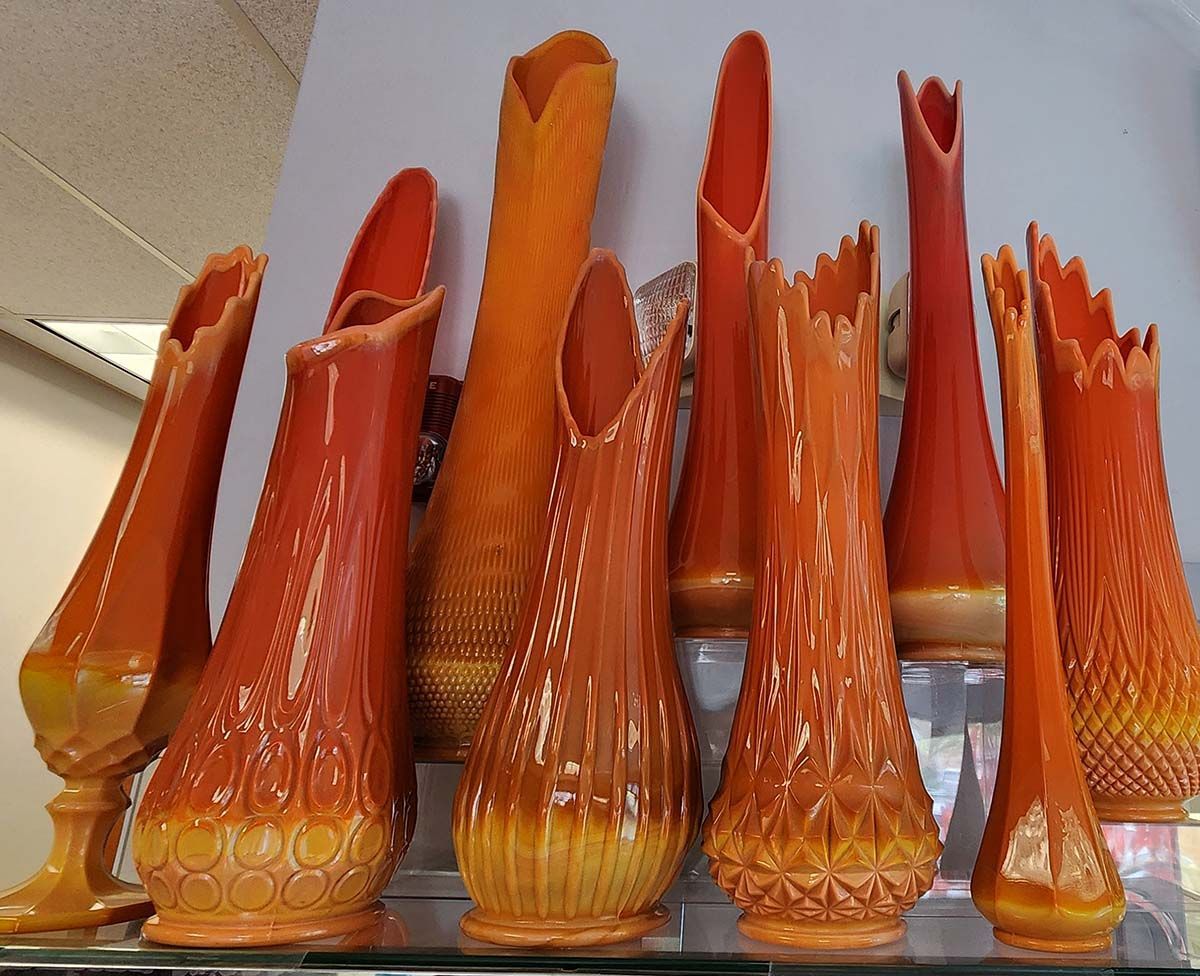 A bunch of orange vases are lined up on a glass shelf