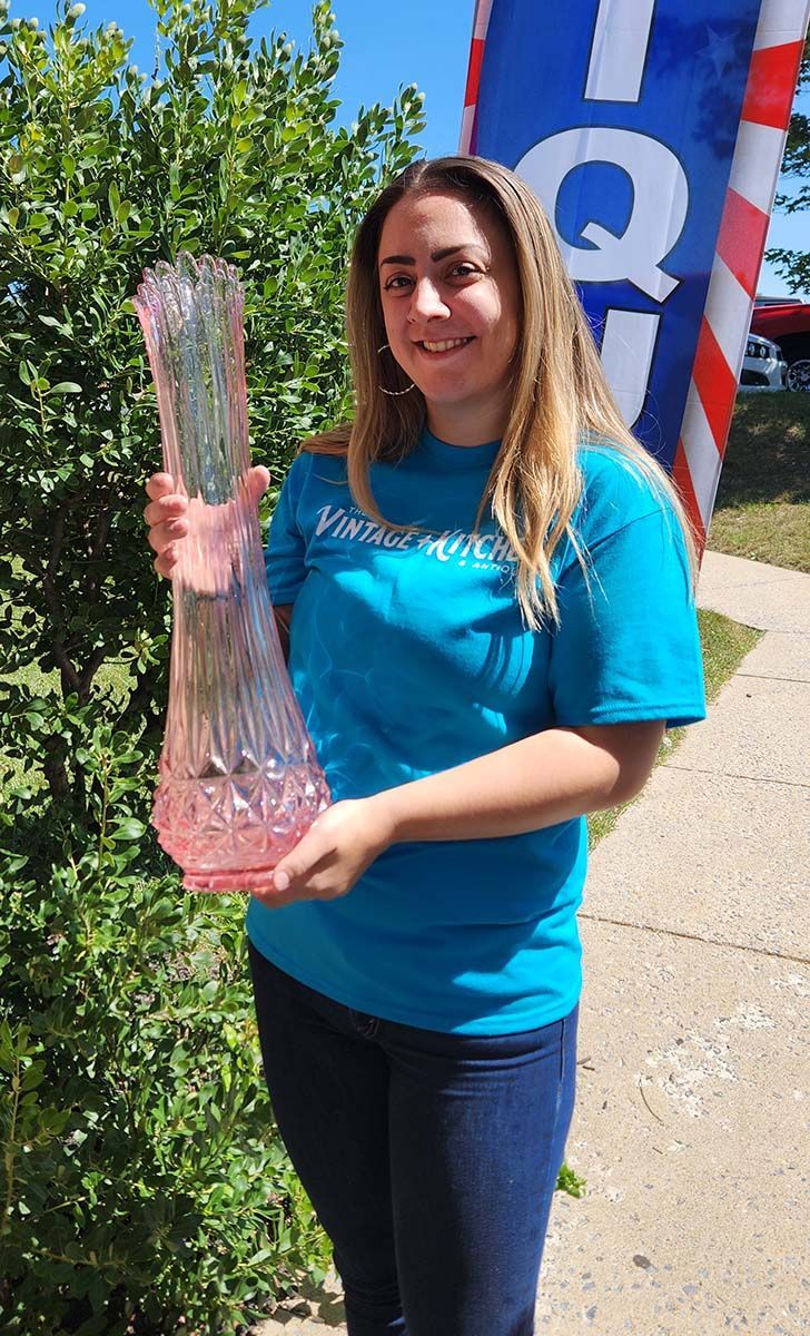 A woman in a blue shirt is holding a pink vase