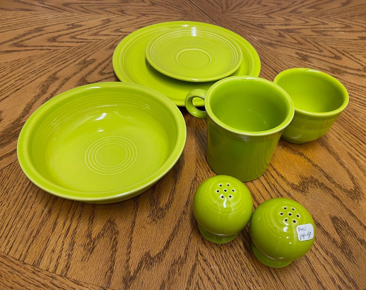 A set of green plates bowls cups and salt and pepper shakers on a wooden table