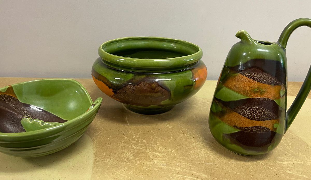 A green bowl a pitcher and a broken bowl are on a table