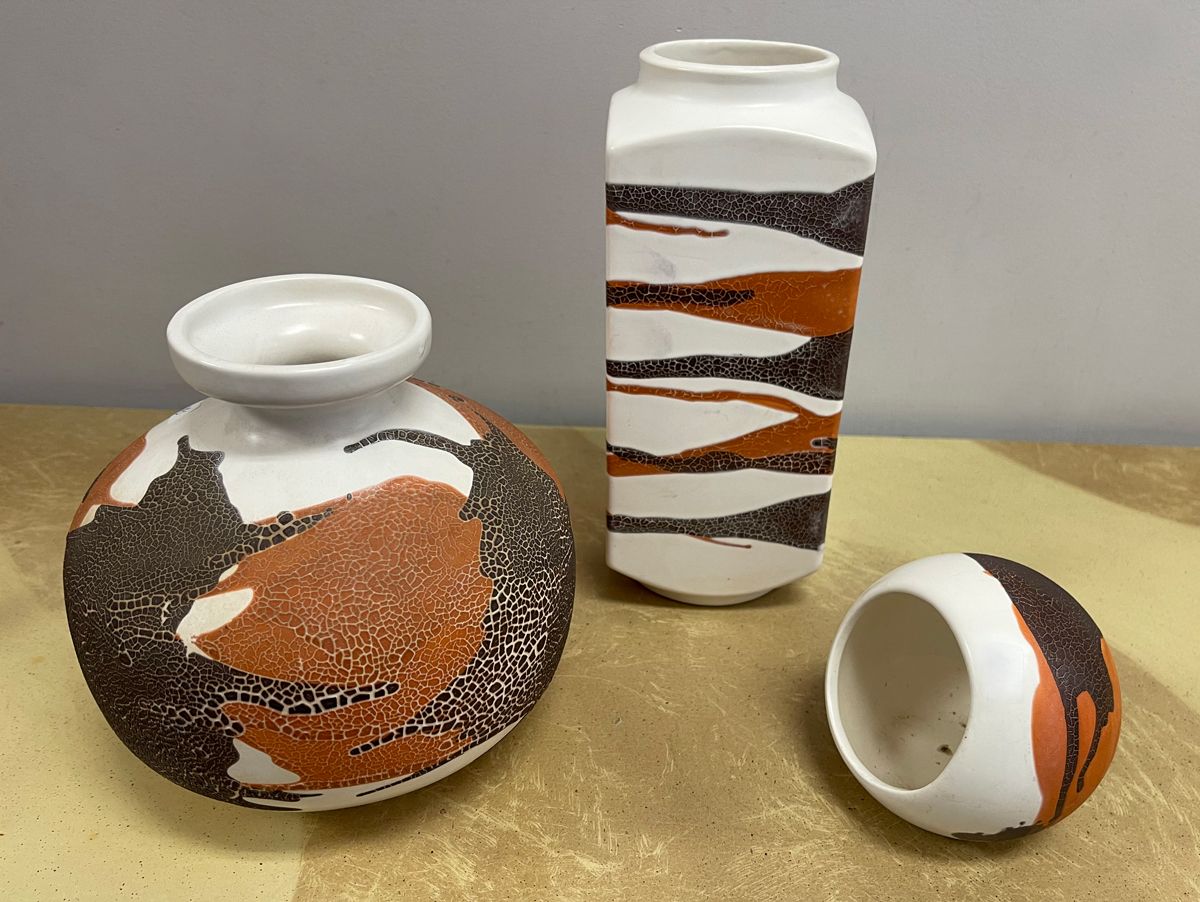 Three vases are sitting on a table with one broken