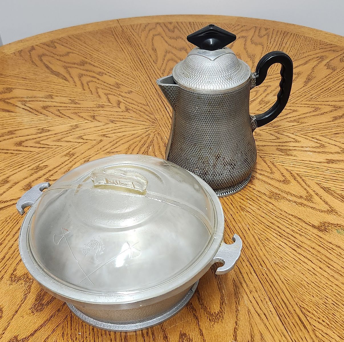 A silver bowl and a silver coffee pot on a wooden table