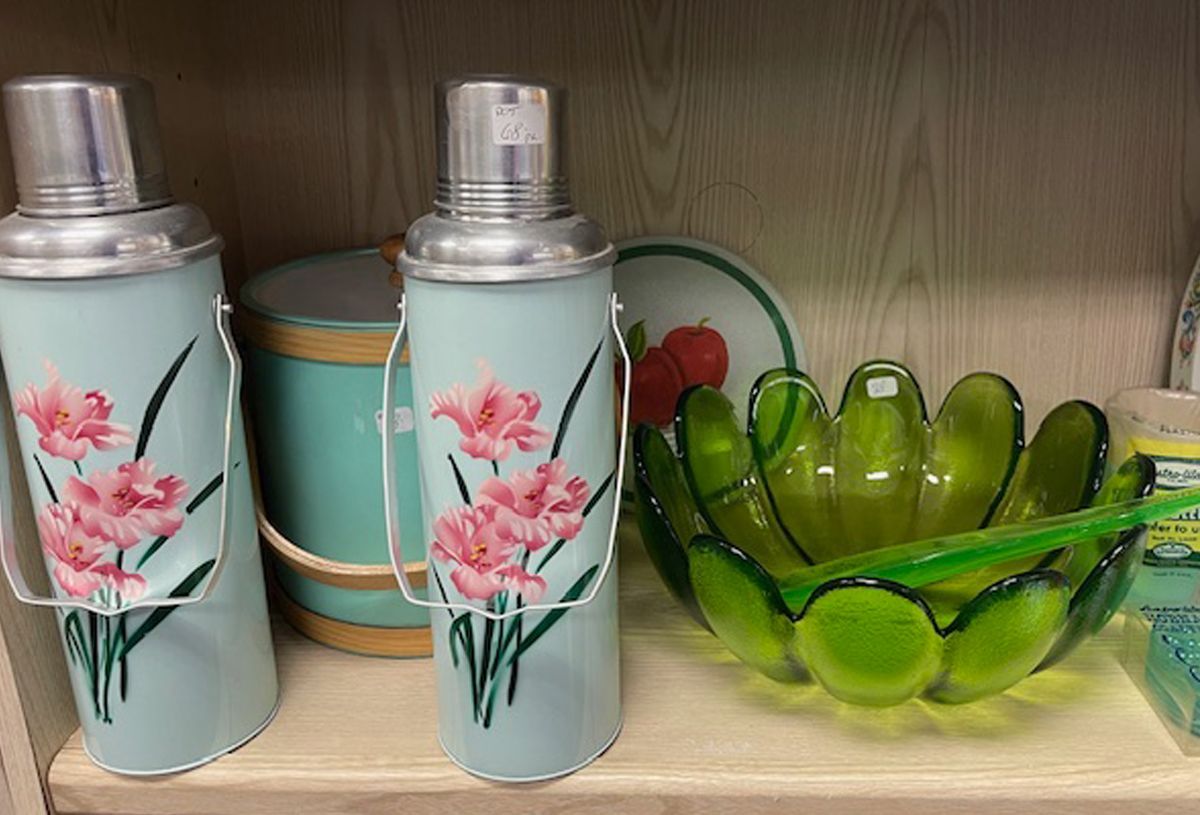 Two thermoses with pink flowers on them are on a shelf next to a green bowl