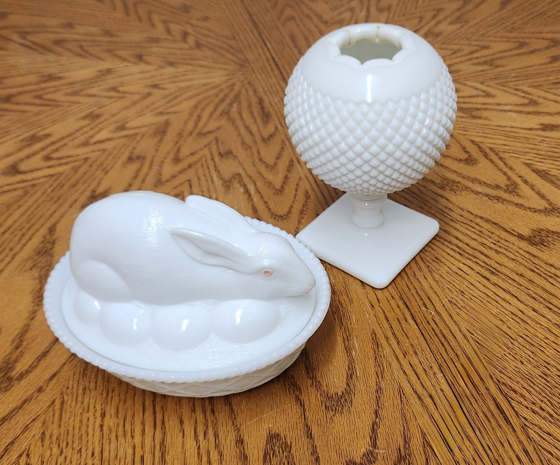 A white rabbit sits on a plate next to a white vase