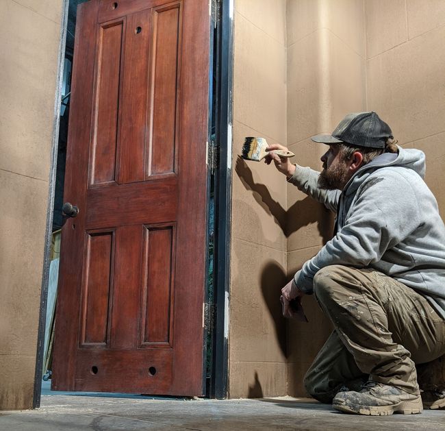 Painting mural with brown wall, wooden door, and kneeling painter.
