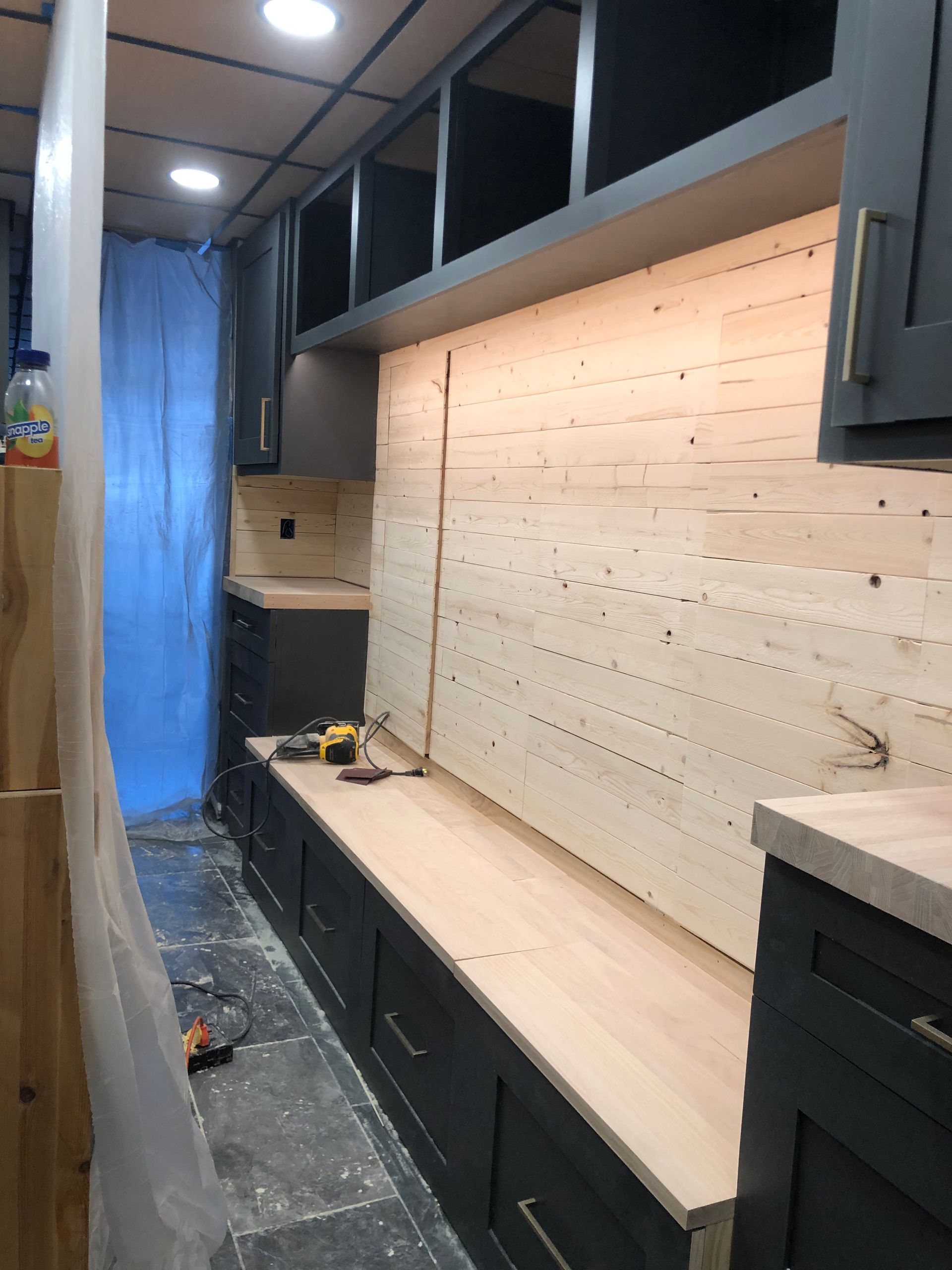 Kitchen renovation with dark cabinets, wood backsplash, and tools.